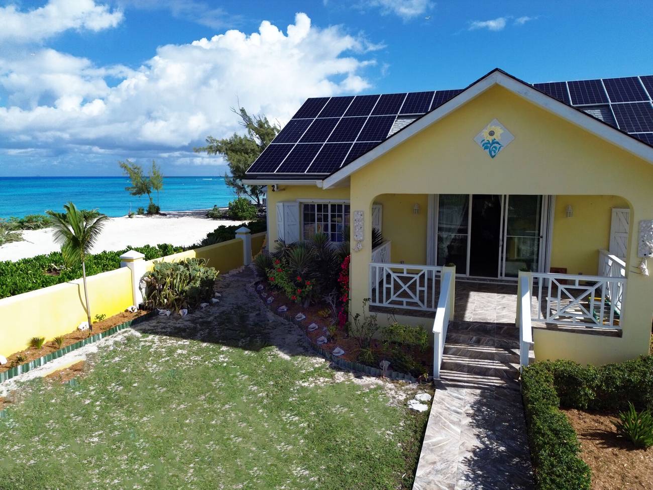 The yellow villa with solar panels, the beach and sea behind it
